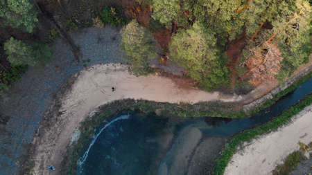 Autumn park view from a drone, the drone descends to the river between the trees, people walk along the path near the shore in the autumn colorful park. The river is bright blue with clear water.の写真素材