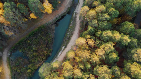 The drone flies over an autumn park with colorful foliage and a beautiful winding river. People walk along the bank of the river enjoying nature and fresh air.の写真素材
