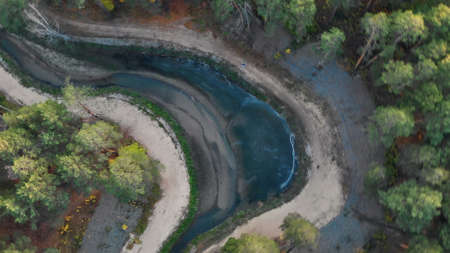 The drone flies over an autumn park with colorful foliage and a beautiful winding river. People walk along the bank of the river enjoying nature and fresh air.の写真素材