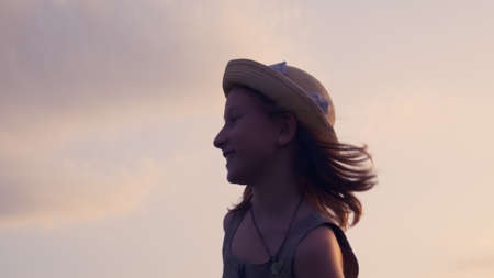 A beautiful teenage girl in a hat on a meadow runs on the grass with an airplane in her hands in the rays of the setting sun. Childhood play and daydreaming. Happy emotions of children.の写真素材