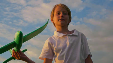 Boy teenager blond in the rays of the setting sun plays with an airplane. He dreams of becoming a pilot. Close up of bright emotions of children.の写真素材