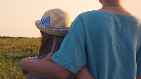 Mother and daughter stand in the meadow of the field in an embrace, the girl has a beautiful greaseproof hat. Relationships in the family, love of mother and daughter in an incomplete family.の写真素材