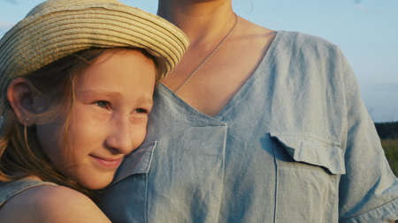 A beautiful blonde girl in a hat clung to her mothers chest. Love for her mother and her children. Childish tenderness.の写真素材