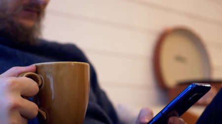 Close-up of coffee mug and smartphone in hands. Morning coffee and latest news in smartphone. A typical morning is not possible without a smartphone and coffee.の写真素材