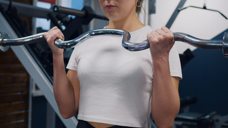 A beautiful woman in the gym pumps her arm muscles with a barbell. Strength training for fat burning...