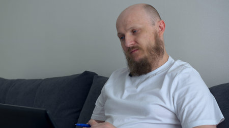 A man works at a computer, conducts business from home, focused on the work he does. A man is focused on the work performed for the customer. Serious man doing complicated calculations.の写真素材