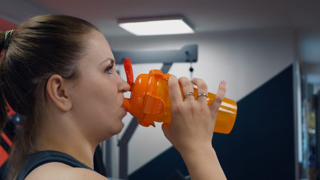 A woman in the gym drinks water from a bottle while relaxing during strength and cardio exercises...
