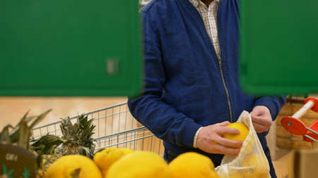 A man in a fruit market chooses a yellow quince. Buying fruits in the supermarket. Ripe fruit nutrition to get vitamins from delicious natural tropical fruits. Nutrition for vegans and fruitarians.の写真素材