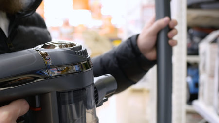 A man in a store chooses a vacuum cleaner, tries to connect the pipe. Buying a vacuum cleaner from...