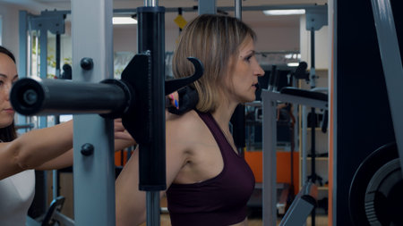 Personal trainer helps to work out in the gym. A woman pumps up the muscles of the buttocks on the...