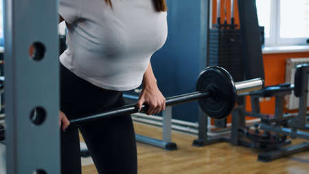 A young woman is engaged in a fitness club according to an individual program. A woman performs a straight-grip barbell row. Exercise is used to develop the back muscles. Woman doing sports exercises.の写真素材