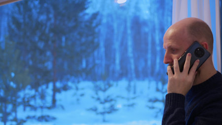 A man at home talking on a smartphone is actively discussing work with a colleague. A bald man is...
