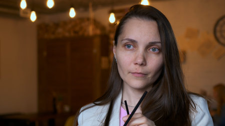 A beautiful woman with a calm expression drinks a cocktail from a straw in a cafe. Waiting for his...