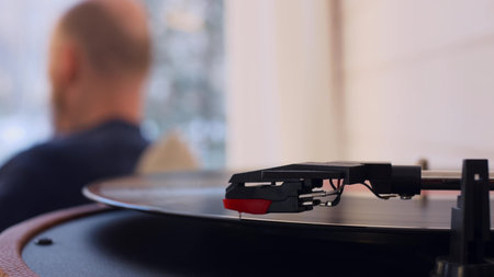 Close-up of a vinyl record spinning in a turntable. In the blurred background, an unrecognizable man...