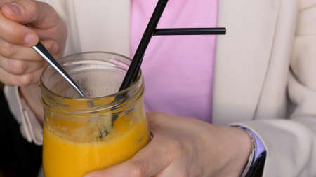 Close-up of a glass cup eating a yellow mango smoothie with a small spoon. Delicious mango smoothie in a cafe, the season of delicious yellow mangoes, sweet as honey. Consumption of fruit smoothies.の写真素材