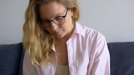 Close-up beautiful blonde woman sitting at home on the couch works remotely via the Internet. A woman with glasses leads a project while sitting at home during a pandemic. Remote learning.の写真素材