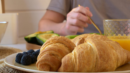 A man has breakfast at home, croissants and fresh berries are on the table. Breakfast before work...