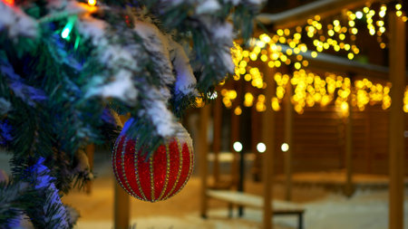 The lights of the garland decorate the house and the Christmas tree, on the branch there is a red sparkling ball. Christmas tree in the evening city on New Years Eve. Christmas mood.の写真素材