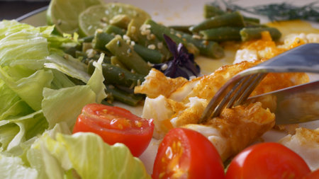 Delicious food for breakfast, classic breakfast of scrambled eggs with fresh vegetables and herbs. Delicious breakfast on a keto diet. Close-up cut an omelet with a fork and knife.の写真素材