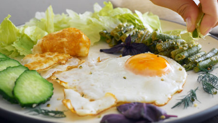 Cinematic footage of a breakfast of fried eggs and fried vegetables and greens. Squeeze a lime wedge over the fried beans. Healthy and hearty breakfast at home or in a restaurant. Proper nutrition.の写真素材