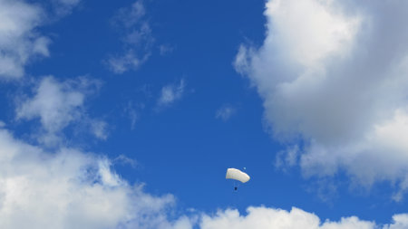 An extreme sport skydiver descends on parachute flying through clouds white wing type parachute. Thirst for adrenaline makes people jump with parachute, for adrenaline rush it causes addiction to fearの写真素材
