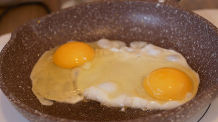 Cooking scrambled eggs for breakfast, another egg is driven into pan for fried eggs. A man cooks...