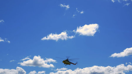 Camera movement from right to left as helicopter flies through blue cloudy sky and descends in preparation for landing. Airplane wing against sky with cumulus clouds. Helicopter is preparing to land.の写真素材