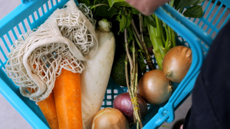 Shopping basket filled with vegetables is held in hand by buyer, top view. Consumer basket of people who can afford fresh vegetables and fruits from an eco-shop. Organic vegetables in shopping cartの写真素材