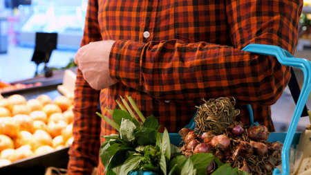 Man picks up an onion from shelf and puts it in shopping basket at grocery store. Buying vegetables at local farmers market. Eating lots onions and vegetables. Buying fresh onions and herbs at marketの写真素材
