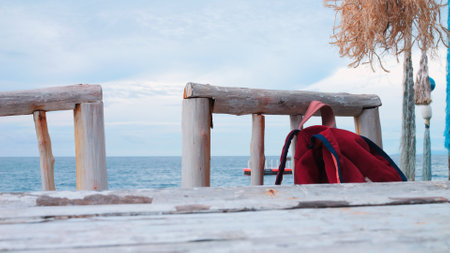 Red backpack lies on sandy beach. Backpack seems small but inside it hides lot of things for relaxing at sea: towels creams beachwear. Concept of travel, vacation, freedom. Traveler backpack on shoreの写真素材