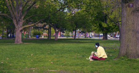 Girl in headphones relaxes with dog in sunlit summer park. Gentle breezes and melodies fill the summer park. Moments of peace, as both find solace in the summer park embrace.の写真素材