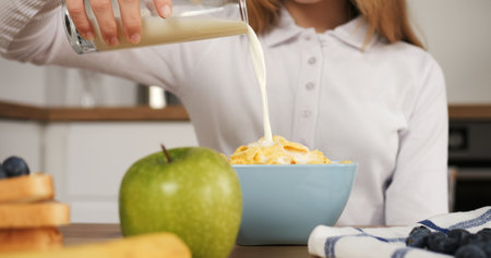 In modern kitchen girl slow pour of milk into cereal healthy eating Cornerstone of day healthy eating moment prepares for school. Focus on healthy eating captured in slow motion close-up.の写真素材