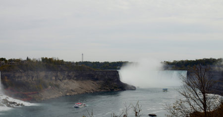 Hydrodynamics of turbulent water flow at Niagara Falls. Majestic view from afar reflects majesty of waterfall and its surrounding natural landscapes, showcasing dynamic flow of water.の写真素材