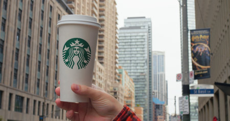 Toronto, Canada - May 6, 2023: Hand holds Starbucks cup, iconic urban backdrop City hustle flows as Starbucks offers familiar comfort. Emblematic coffee moment in metropolitan life. Starbucks conceptのeditorial素材
