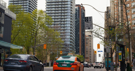 Toronto, Canada - May 6, 2023: Toronto daily hustle. Orange taxi amidst flow of cars on busy streets, urban landscape with modern skyscrapers towering over downtown, true North American city life.のeditorial素材
