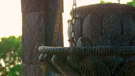 Close-up of weathered stone sculpture, delicately hanging from chains, illuminated by the soft glow of the setting sun. ornamental piece represents the timeless beauty of traditional craftsmanship.の写真素材