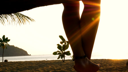 Woman swings gently on tropical beach at sunset, her silhouette blending into serene scene. Perfect moment of relaxation and tranquility in paradise setting, ideal for vacations.の写真素材