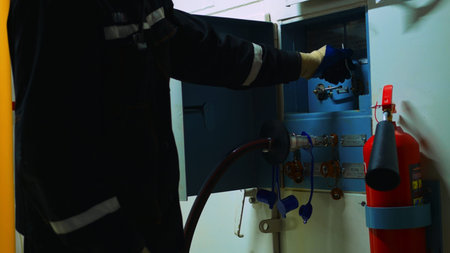 Industrial worker in protective gear operated valve on control panel, with fire extinguisher in...
