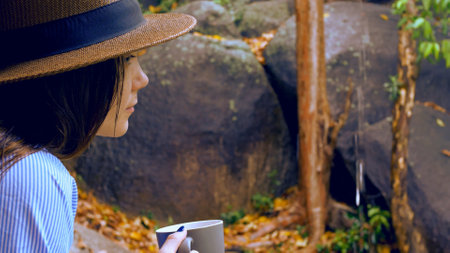 Woman enjoys peaceful moment sipping tea in nature on calm autumn day. Scene captures relaxation, solitude, and mindfulness. Soft rain enhances peaceful mood, ideal for themes of reflection.の写真素材