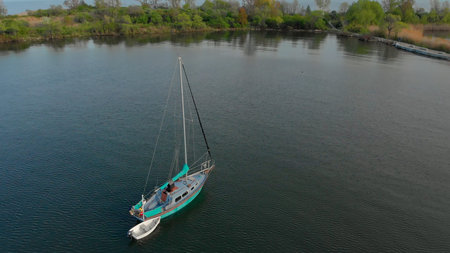 Yacht rest peacefully on lakes surface, embraced by green shores. Calm water and lush landscape make...