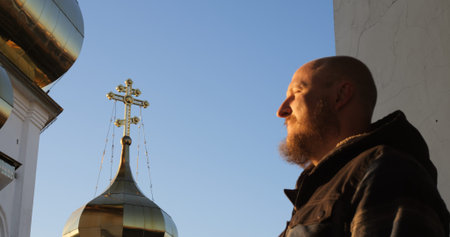 Bearded man performs sign of cross with Orthodox church domes in background, emphasizing spirituality, sacred rituals, and cultural heritage in a tranquil religious setting. Man crossing himselfの写真素材