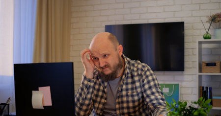 Remote professional with beard working at home office desk, managing digital documents and typing on laptop, representing contemporary telecommuting lifestyle. Home accounting conceptの写真素材