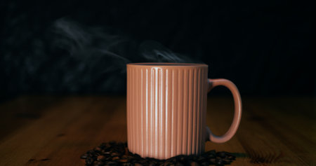 Moody close-up focusing on ceramic mug emitting gentle steam, mug emphasizing handcrafted shape and warm ambiance.の写真素材