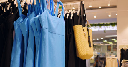 Bright blue sundresses and yellow beach bag hanging neatly on clothing rack, showcasing summer fashion variety within stylish retail interior. Concept fashion clothesの写真素材