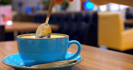 Professional barista carefully stirring creamy cappuccino in elegant blue ceramic cup, resting on...