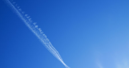 White trail gradually forming across clear blue sky, creating ethereal brushstroke like pattern against atmospheric canvas of pristine daytime environmentの写真素材
