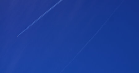 Pristine white airplane contrail stretching across vibrant deep blue sky, revealing aerial journey through cloudless atmospheric expanse during daytime flightの写真素材