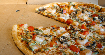Several images showing a delicious shrimp pizza with tomatoes, mushrooms and pesto being sliced and a slice being taken from the cardboard boxの写真素材