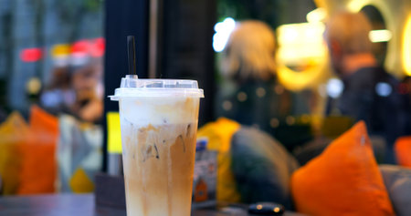 Relaxed young professional sipping chilled coffee with creamy topping at sunlit sidewalk cafe, capturing casual urban lifestyle momentの写真素材
