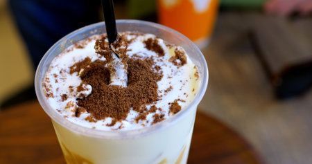 Skilled barista sprinkling cocoa powder over whipped cream, creating artistic latte design with precise dark straw garnishing techniqueの写真素材